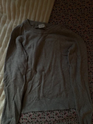 Grå stickad tröja från Vila - En enkel och stilren grå stickad tröja från Vila. Tröjan har rund halsringning, ribbade muddar vid ärmslut och nederkant samt lång ärm🩷Säljer för att jag inte använder den💕 Tröjan är i mycket bra skick och känns oanvänd🩷