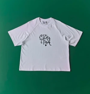 Mertra - Vit t-shirt från mertra med coolt camo-mönstrat tryck på bröstet. Modellen har korta ärmar och en klassisk rund halsringning. Materialet känns mjukt och lätt, perfekt för dig som gillar streetwear med en twist.