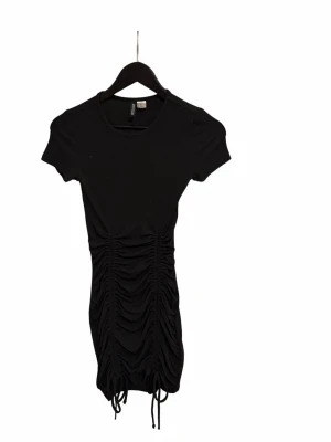Svart kortklänning med snörning - Snygg svart kortklänning från Divided med korta ärmar och snörningsdetalj framtill som ger en rynkad effekt.  tight passform 