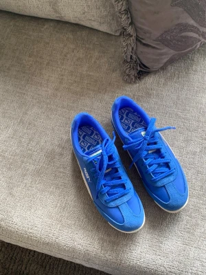 Blå sneakers från Puma - Säljer ett par nya snygga blå sneakers från Puma med vit sula och klassisk logga på sidan. Skorna har snörning och är tillverkade i en mix av mocka och syntetmaterial. Perfekta för dig som vill ha en sportig och stilren look.