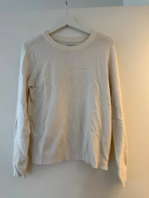 Vit stickad tröja från VILA - En enkel och stilren vit stickad tröja från VILA. Tröjan har rund halsringning, ribbade muddar vid ärmslut och nederkant samt lång ärm. Perfekt att slänga på sig under kyligare dagar.