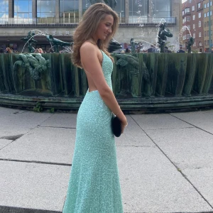 Mintgrön glittrig långklänning - Säljer en mintgrön långklänning med paljetter som ger ett riktigt glittrigt intryck. Klänningen har öppen rygg och smala axelband, perfekt för bal eller fest. Materialet är syntet och klänningen har en figurnära passform.