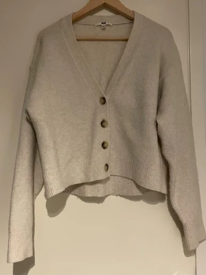 Vit kofta från Uniqlo - Mysig beige kofta från Uniqlo i storlek XS. Koftan har v-ringning, fyra stora knappar framtill och är långärmad. Materialet känns mjukt och lite fluffigt, perfekt för lager på lager under kyliga dagar. Den är lite nopprig!