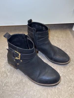 Svarta boots med spänne i skinn - Säljer ett par svarta boots i skinn med guldfärgade spännen och dragkedja på sidan. 