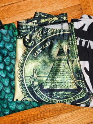 BlackMilk 2st leggings XS, 1st leggings zebra okänt märke - Två par leggings från BlackMilk i storlek XS. Ena paret har ett grönt fjällmönster som påminner om sjöjungfru, det andra har ett dollartryck med pyramid och öga. Båda är i stretchigt syntetmaterial och sitter tight mot kroppen. 3 paret är zebra mönstrade med röda inslag i storlek S Sparsamt använda