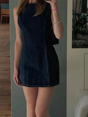 Mörkblå jeansklänning från Zara - Säljer en snygg ärmlös jeansklänning från Zara i mörkblå denim. Klänningen är kort, har en rund halsringning och markerade sömmar som ger en schysst passform. Den har använts en gång bara. 