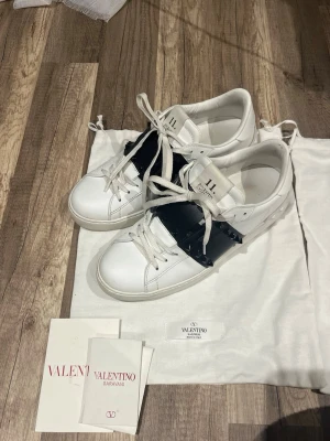 Valentino Rockstud sneakers vit/svart - Säljer ett par Valentino Garavani Rockstud sneakers i vitt skinn med svart band och nitar över vristen. Kommer med dustbag och originalpapper, även kvitto. Jag har använt dom 3 gånger, och den ända tecken på användning är att piggarna under sulan inte är lika spetsiga. Annars mycket bra skick. 