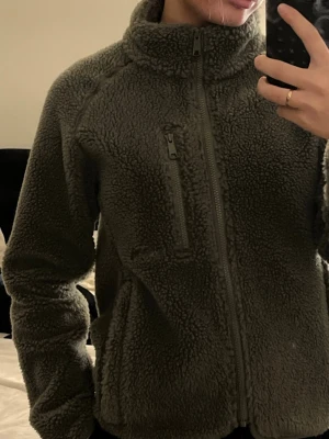 Militärgrön teddyjacka  - Säljer en militärgrön teddyjacka från märket Tretorn med hög krage och hel dragkedja framtill. Jackan har en bröstficka med dragkedja och två sidofickor. Perfekt för kalla dagar och riktigt mysig att bära. Den har innerfickor med. Har använts 1 gång. 