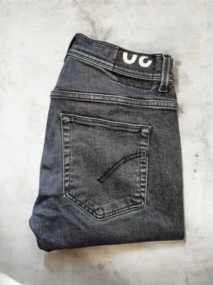Stentvättade Dondup Konor jeans, storlek 30 - Svarta stentvättade Dondup jeans, modell Konor i Skinny Fit. En stilren och modern jeansmodell från det italienska premiumvarumärket Dondup, perfekt för en tajt och välsittande silhuett.  Jeansen är i mycket bra skick. Enda anmärkningen är att lappen har försvunnit, i övrigt finns inga hål eller andra defekter.   Storlek: 30  Mått: 1/2 midja: 38 cm Längd: 98 cm Lårbredd: 24 cm                                                   Benöppning: 15 cm