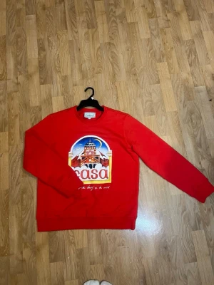 Casablanca hoodie/sweatshirt - Säljer en röd sweatshirt från Casablanca med stort färgglatt tryck framtill som föreställer ett hus och texten 'casa'. Tröjan har rund halsringning och långa ärmar. Perfekt statement-plagg för dig som gillar unika prints.