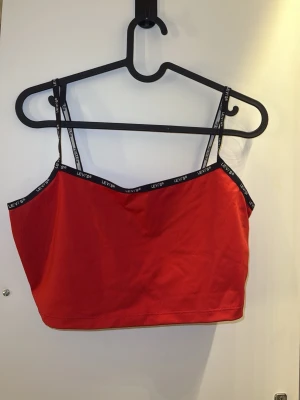 Röd linnetopp från Levi's - Säljer en röd linnetopp från Levi's med tunna axelband och svart kantband med logga runt om. Toppen är croppad och passar även till S och Xs!
