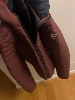 Pufferjacka Colmar - Säljer en vinröd pufferjacka från Colmar Originals i storlek 50. Jackan har huva, två fickor med dragkedja och quiltad design. Materialet är syntet och jackan har en mörkblå insida. Perfekt för kalla dagar! Modellen är ca 180 och väger ca 80 kg