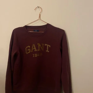 Gant tröja  - Säljer en långärmad Gant tröja som är vinröd. Knappt använd. Gulldig text som glittrar lite. ordinarie pris är 1000. Säljer den för 100