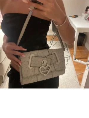 Guess väska – superfin 🤍✨ - Säljer en jättefin Guess-väska i ljusgrå/beige ton med silverdetaljer och hjärtformat Guess-lås 🤍 Perfekt storlek till vardag eller fest, rymmer mobil, plånbok m.m. Använd men i fint skick. 📦 Kan skickas direkt 💬 Pris kan diskuteras vid snabb affär ⚡ Först till kvarn!