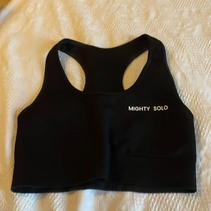 Svart träningsväst från Mighty Solo - Säljer en svart träningsväst från Mighty Solo med brottarrygg och logga framtill. Västen är tillverkad i stretchigt material (90% nylon, 10% spandex) och har en stilren look utan mönster. Perfekt för gymmet eller löprundan.Endast provad så i nyskick.