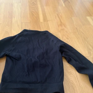 Svart ribbad långärmad tröja XS/S - Svart långärmad tröja från NEH Apparel i ribbat material. Tight passform och rund halsringning, perfekt för träning eller som basplagg. Diskret logga på bröstet och stretchigt tyg som sitter snyggt på kroppen. Jätte nice till gymmet!