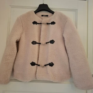 Beige teddyjacka från Gina Tricot XS - Supermjuk och fluffig teddyjacka i beige från Gina Tricot. Jackan har coola svarta detaljer och tre snygga spännen framtill. Perfekt för dig som vill ha en mysig och trendig look under kyliga dagar. St xs rymlig i storlek. I toppen skick 