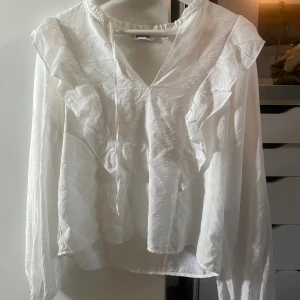 Vit volangblus från Kappahl - Supersöt vit blus från Kappahl med volangdetaljer längs axlarna och v-ringning med knytband. Knappast använd med har en defekt på bild 3, men absolut inget man märker när den sitter på💗