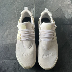 Vita Nike Presto sneakers - Säljer ett par fräscha vita Nike Presto sneakers med klassisk mesh-överdel och tydlig swoosh på tån. Skorna har snörning, platt sula och en clean, sportig look. Perfekta för dig som gillar stilrena och bekväma sneakers med modern känsla. Nästan helt nya, inga skador eller slitna. Bara lite smutsiga men det går att rengöra hur lätt som helst