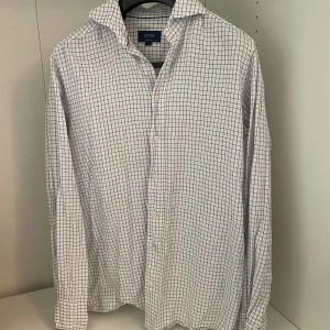 Vit rutig skjorta från Eton, M - Knappt använd och nypris 1700kr.                       Vit skjorta från Eton i storlek M med blått rutmönster. Klassisk krage, långärmad och knäppning framtill. Skjortan är tillverkad i bomull och har en modern, stilren look som passar perfekt till jeans eller chinos.
