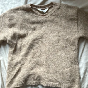 Beige stickad tröja från H&M - Mysig beige stickad tröja från H&M med rund halsringning och ribbade muddar. Perfekt för lager-på-lager under hösten och vintern. Enkel och stilren design som passar till allt.