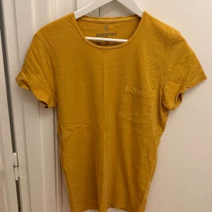 Gul t-shirt från Blueprint i bomull - Snygg gul t-shirt från Blueprint med rund halsringning och en liten bröstficka. T-shirten är i mjuk bomull och har korta ärmar. Perfekt för dig som gillar enkel och stilren design med en poppig färg. Storlek M.