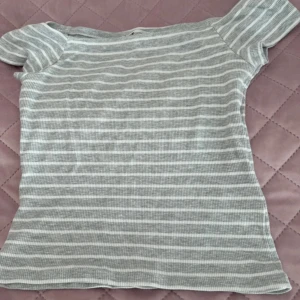 Randig ribbad topp från FB Sister - Grå och vit ribbad topp från FB Sister i storlek L. T-shirten har korta ärmar och ett klassiskt randigt mönster. Materialet är mjukt och stretchigt, perfekt för en chill och enkel look🩷