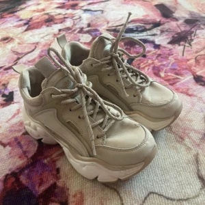 Beige chunky sneakers från Buffalo strl 36 - Buffalo sneakers i beige med chunky plattformssula och snörning. Veganskt material och cool retrostil. Ovandel i syntet och textil, detaljerad sula med transparenta partier undertill. Perfekta för dig som gillar statement-skor! Okej skick, se bilder. 