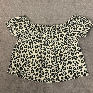 Leopardmönstrad offshoulder topp Gina Tricot - Säljer en snygg offshoulder topp från Gina Tricot i leopardmönster. Toppen är beige med svarta fläckar, har korta puffärmar och resår vid axlarna för en trendig look. Perfekt för dig som vill sticka ut lite extra. Säljer pågrund av att den är oanvänd. 