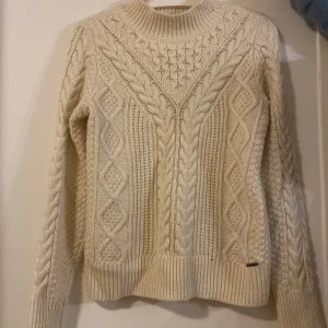 Beige stickad tröja Abercrombie S - Säljer en chunky beige stickad tröja från Abercrombie & Fitch i storlek S. Tröjan har grovt flätmönster, ribbade muddar och hög hals. Perfekt för kyliga dagar och riktigt snygg till jeans eller kjol.