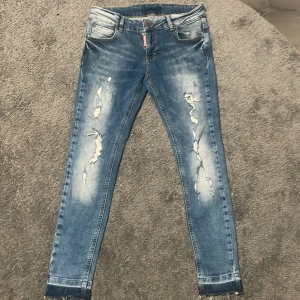 Blå jeans från Dsquared2 - Snygga blå slim  jeans från Dsquared2 med slitningar på benen och fransade benslut. Jeansen har klassisk femficksdesign, Dsquared2-logga på fickan och knapp, samt en röd etikett vid gylfen. Perfekt för dig som gillar en trendig och edgy look.