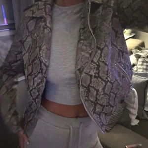 Grå ormmönstrad bikerjacka NA-KD - Säljer en grå och svart ormmönstrad bikerjacka från NA-KD. Jackan har klassisk krage, dragkedjor i silver och två fickor framtill. Endast använd en gång! 