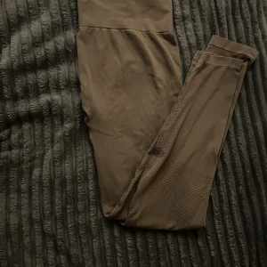 Bruna träningstajts - Ett par bruna träningstajts som är i bra skick förutom texten i där tvättråd och storlek står. Byxorna fungerar bra att tvättas som vanliga träningsbyxor och jag skulle gissa att storleken är ungefär xs/32-34. Varan har ganska hög midja men fungerar utmärkt att vika ner till önskad längd. Gjord i ett stretchigt material som passar utmärkt till fysisk aktivitet.