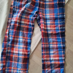 Rutig pyjamasbyxa från Björn Borg M - Färgglada pyjamasbyxor från Björn Borg i storlek M. Byxorna har ett rutigt mönster i blått, rött, orange och vitt, med resår i midjan för extra komfort. Perfekta för att chilla hemma eller sova i. Tillverkade i mjuk bomull.
