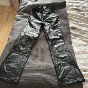 Svarta bootcut byxor i skinnimitation - Snygga svarta byxor från Bik Bok i skinnimitation med bootcut-ben. Byxorna har klassisk femficksdesign, dragkedja och knapp framtill. Perfekta för dig som vill ha en edgy look med lite glansig finish. Som nya.