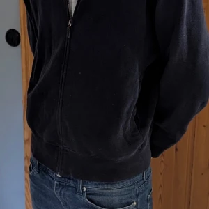 Marinblå hoodie från Polo Ralph Lauren M - Marinblå hoodie från Polo Ralph Lauren i 100% bomull. Klassisk design med dragkedja framtill, två fickor och rött broderat logomärke på bröstet. Långärmad och normal passform, perfekt för en chill och stilren look.