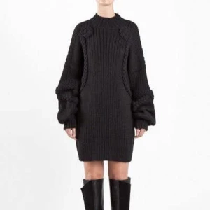 Svart stickad tröja/klänning från Carin Wester - Svart stickad tröja från Carin Wester med oversized passform, ballongärmar och flätade detaljer längs ärmar och sidor. Ribbstickad struktur och hög hals. Kan ävrn användas som klänning. Materialmix av ull, alpacka, bomull och syntet. Perfekt för dig som gillar statement-plagg med cool siluett. Inga anmärkningar, mycket fint skick utan noppor. 