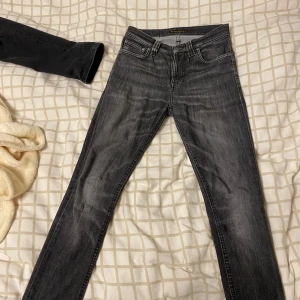 Svarta skinny jeans från Nudie Jeans - Säljer ett par mörk gråa skinny jeans från Nudie Jeans. Jeansen har en mörk tvätt och råa kanter vid bensluten. Perfekta för dig som gillar en smal passform och stilren look.