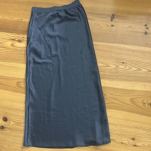 Svart satinkjol i lång modell - Snygg svart långkjol i satin med slät, glansig yta och enkel, rak passform. Kjolen har en minimalistisk look och faller snyggt längs kroppen. Perfekt för dig som gillar stilrena och trendiga plagg. Den är från Gina och i storlek xs. Har andvänt en gång och ny pris är 400kr