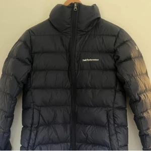 Mörkblå dunjacka Peak Performance - Säljer en Mörkblå dunjacka från Peak Performance med hel dragkedja framtill. Jackan är quiltad och har diskret logga på bröstet och ärmen. Perfekt för kalla dagar och har en klassisk, stilren look. Priset går självklart att diskutera 