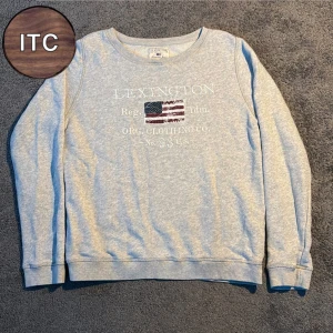 Lexington sweatshirt - Snygg grå sweatshirt från Lexington med amerikansk flagga och vit text framtill. Tröjan har rund halsringning och långa ärmar, perfekt för en chill och avslappnad stil. Tillverkad i mjuk bomull för extra komfort.