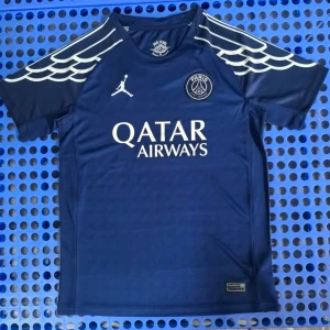 PSG x Jordan blå fotbollströja - Snygg marinblå PSG fotbollströja från Jordan med vita detaljer och vingar på axlarna. Tröjan har korta ärmar, rund hals och Qatar Airways-tryck på bröstet. Perfekt för dig som älskar fotboll och streetwear.