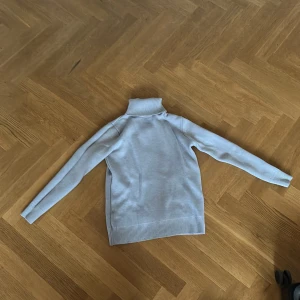 Ljusgrå polotröja med ribbade detaljer - Snygg ljusgrå polotröja med lång ärm och ribbade muddar vid ärmslut, nederkant och krage. Perfekt för kyligare dagar och enkel att matcha med olika outfits. Mjuk och skön känsla.