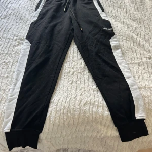 Svart mjukis sett  från Elly Pistol - Svart mjukis sett  från Elly Pistol med vita detaljer längs ärmarna och stor vit logga på ryggen. Tröjan har huva med snörning, half zip och en stor ficka framtill. Materialet är mjukt och känns som bomull, perfekt för chill eller träning. Finns att köpa för sig om man vill de istället 