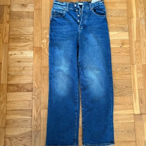 Blå raka jeans från Zara, strl 36 - Snygga blå jeans från Zara i rak modell med hög midja och knäppning framtill. Jeansen har klassisk femficksdesign och är tillverkade i ett robust denimtyg. Perfekta för dig som gillar en avslappnad och trendig look.