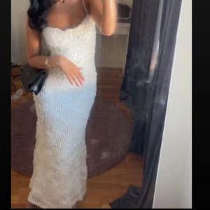 Vit långklänning med spetsdetaljer - Säljer en elegant vit långklänning med tunna axelband och v-ringad urringning. Klänningen har ett snyggt spetsmönster och figurnära passform som ger en riktigt chic siluett. Perfekt för dig som vill sticka ut med en stilren look. Materialet känns lyxigt och har fina detaljer.