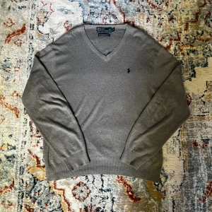 Tröja från Polo Ralph Lauren - Klassisk grå v-ringad tröja från Polo Ralph Lauren med broderad marinblå logga på bröstet. Använd ett tag, men trots det i ett mycket bra skick.