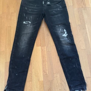 Jeans från Lorenzo veratti  - Svarta jeans från Lorenzo Veratti, storlek S. Snyggt slitna med detaljer som dragkedja vid anklarna och lite färgstänk som ger en cool look. Jeansen har tydliga slitningar vid knän och lår, samt ett nyckelclip från Synaworld vid bältesslingan som kommer att medfölja i beställningen. 