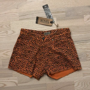 Leopardmönstrade shorts från Von Dutch - Snygga orangea shorts från Von Dutch med svart leopardmönster. Klassisk femficksmodell med kanter och logga tryckt baktill i midjan. Helt nya med tag. Ganska små i stl, tippar mer på XS. 