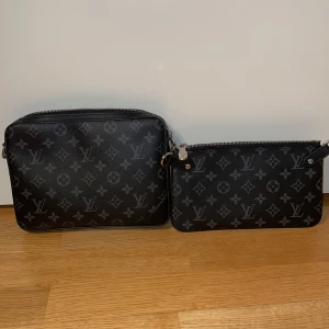Louis Vuitton svart axelväska med monogram - Säljer en svart axelväska från Louis Vuitton med klassiskt monogrammönster i grått. Väskan har flera delar, inklusive en mindre pouch och en liten plånbok, alla med dragkedja. Justerbar axelrem med Louis Vuitton-tryck. Perfekt för dig som gillar stilren och lyxig design. PRIS KAN DISKUTERAS VID SNABB AFFÄR!